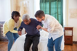 Two people help an elderly man stand up